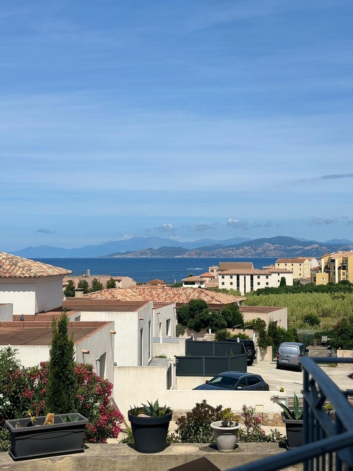 Ein Wohngebiet mit Häusern mit Terrakotta-Dächern, Blick auf das Meer und eine entfernte Bergkette.