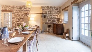 A dining area with a stone wall, wooden table, and chairs. There is a pitcher, plates, and glasses on the table.