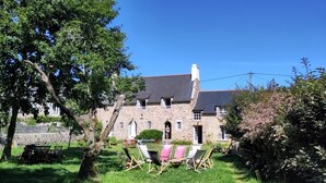 A stone building with a large tree in the foreground, a grassy lawn, and outdoor seating.