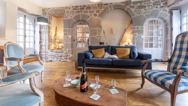 A cozy living room with a stone wall, a blue sofa, and a wooden coffee table with wine glasses and a bottle.