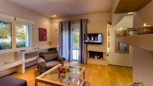 A modern living room with a sofa, a glass coffee table with fruit, a flat-screen TV, and a fireplace. - Aquarius - Glyfada Detached House (Glyfada)