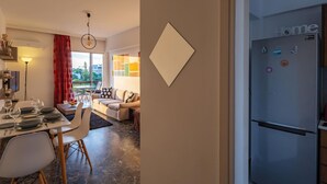 A modern kitchen with a stainless steel refrigerator, a dining area with a table set for two, and a living area with a sofa and a coffee table. - Archer - Sea View Apartment (Vari-Voula-Vouliagmeni)