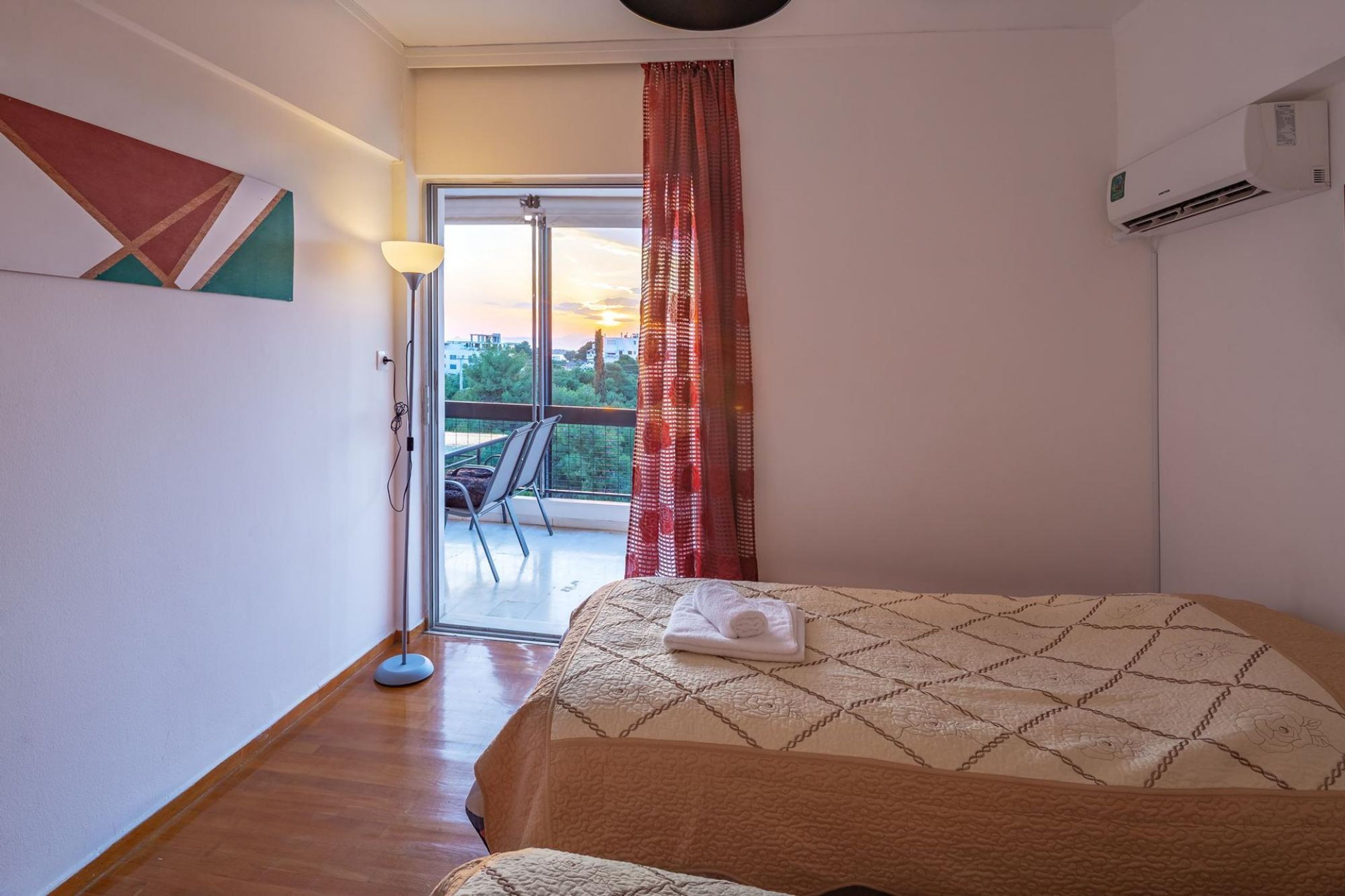 A hotel room with a bed, a floor lamp, a view of the outdoors, and an air conditioning unit.