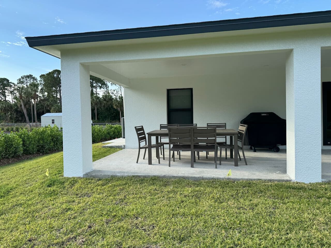 A covered patio with a table and chairs, a grill, and a window.