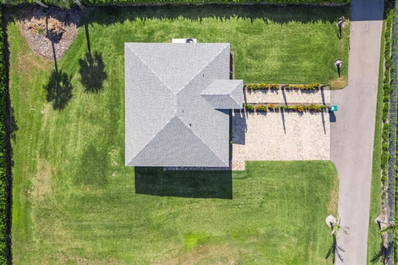 An aerial view of a building with a large, flat roof, surrounded by a well-maintained lawn and a paved driveway.