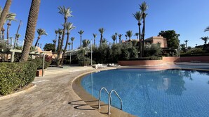 Ein Poolbereich mit klarem, blauem Pool, Palmen und einem Gebäude im Hintergrund.