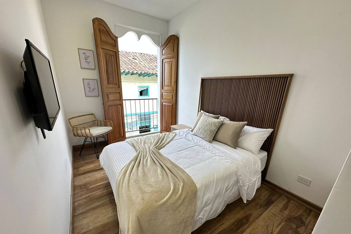 A bedroom with a bed, a chair, a TV, and a balcony view.