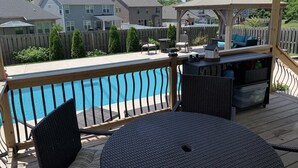 Een overdekt terras met een zwembad, tuinmeubilair en een tuinhuisje.