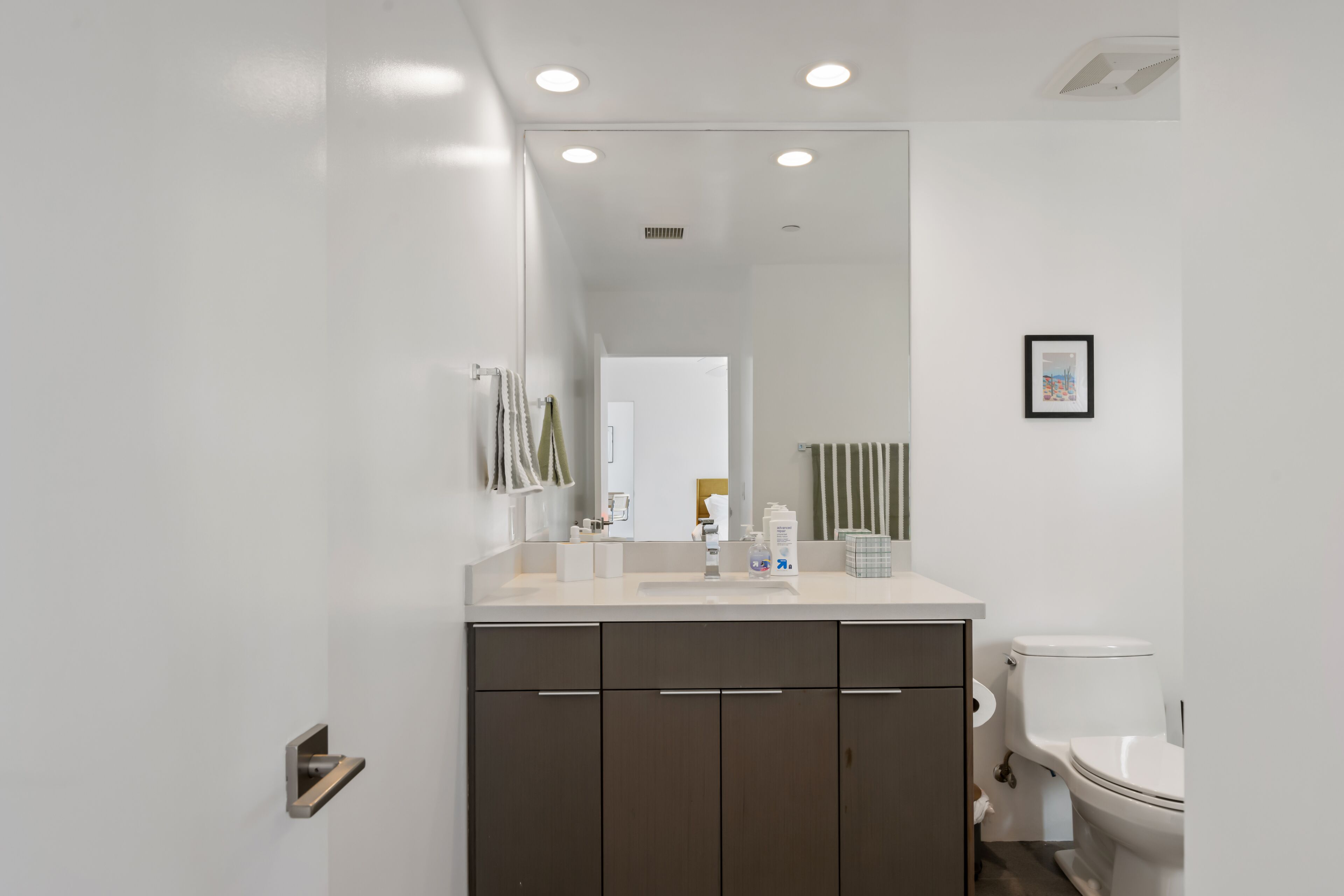A modern bathroom with a white sink, dark cabinets, a toilet, and a mirror.