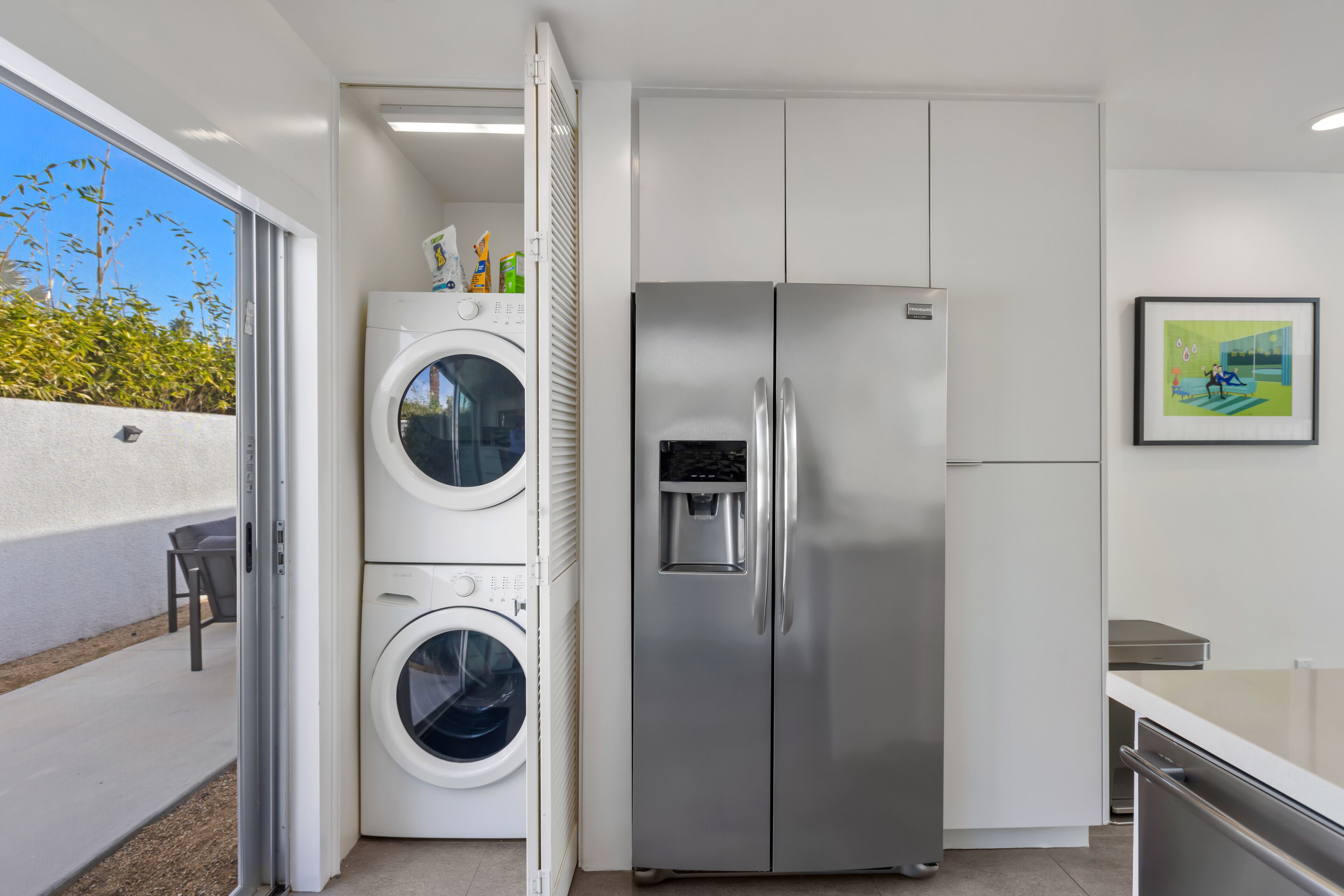 A compact kitchen with a stainless steel refrigerator, a built-in washing machine, and a small dining area with a table and chairs.