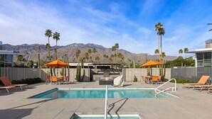 A pool area with lounge chairs and umbrellas, surrounded by palm trees and mountains in the background. - Come visit Palm Springs! (Palm Springs)