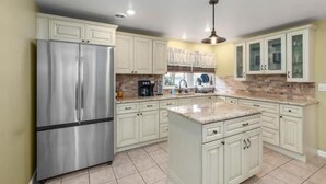 A kitchen with white cabinets, a stainless steel refrigerator, a granite countertop, and a hanging light fixture.