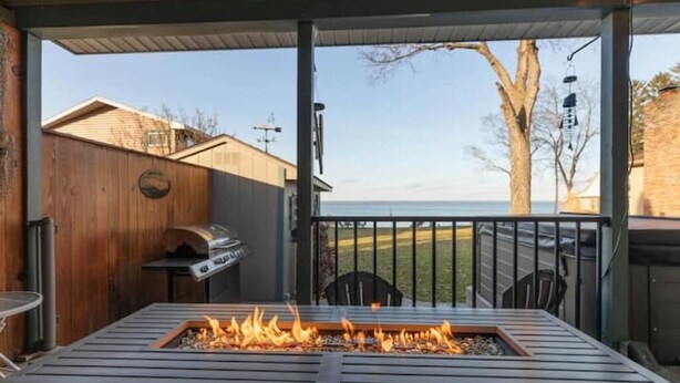 A wooden deck with a built-in fire pit, a grill, and a view of the ocean.