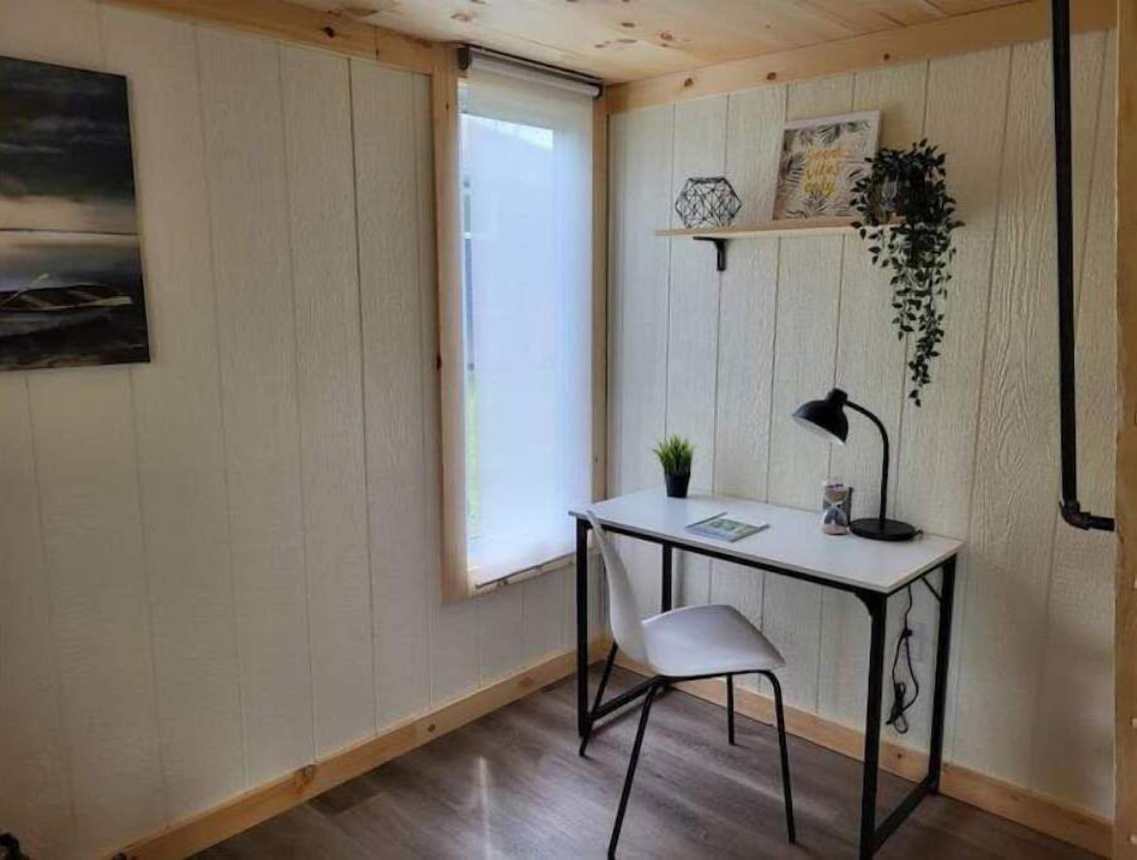 A small, well-lit room with a desk, chair, and a window with blinds.