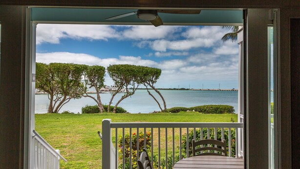 A view from a porch with a wooden railing, overlooking a body of water, trees, and a distant shoreline.