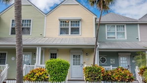 A row of three-story houses with a white picket fence, a front porch, and a small front yard with plants.