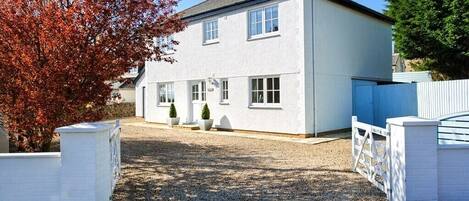 A two-story house with a gravel driveway and a white fence.