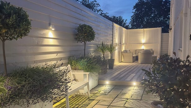 A well-lit outdoor patio area with a stone floor, white walls, and several potted plants. - Ty Coed (Pwllheli)
