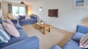 A living room with two blue sofas, a wooden coffee table, and a large window with curtains. - Ty Coed (Pwllheli)