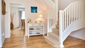 A staircase with white railings leading to a landing, a hanging woven light fixture, and a white console table with drawers and shelves. - Ty Coed (Pwllheli)