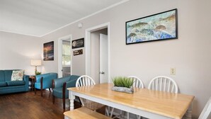 Un área de comedor con una mesa de madera y sillas blancas, un sofá azul y un cuadro en la pared.