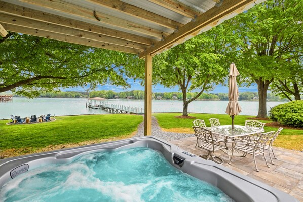Relax in the serene hot tub surrounded by a pergola, lawn, and tranquil lake views.