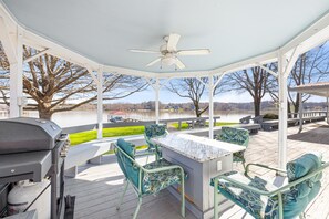 Relax outdoors with a grill, ceiling fan, and comfortable seating area overlooking the water and lush surroundings.