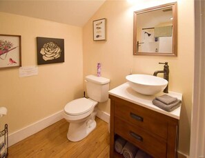 Ein Badezimmer mit Toilette, Waschbecken und einem Holz-Waschtisch. An der Wand befinden sich Bilder in Rahmen.