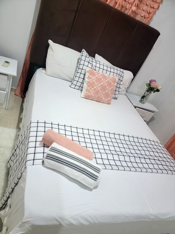 A neatly made bed with a white and black checkered bedspread, a pink pillow, and a white towel.