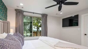 A bedroom with a bed, a ceiling fan, a TV mounted on the wall, and a window with curtains. - Lakeside | Hot Tub | Private Dock | Views (Hot Springs)