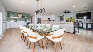 A modern kitchen with white cabinets, a dining area with a glass table and white chairs, and a ceiling fan. - Lakeside | Hot Tub | Private Dock | Views (Hot Springs)