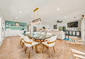 A modern kitchen with white cabinets, a glass dining table, and a unique pendant light.