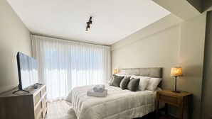 Ein ordentlich eingerichtetes Schlafzimmer mit Bett, Fernseher und Nachttisch mit Lampen.