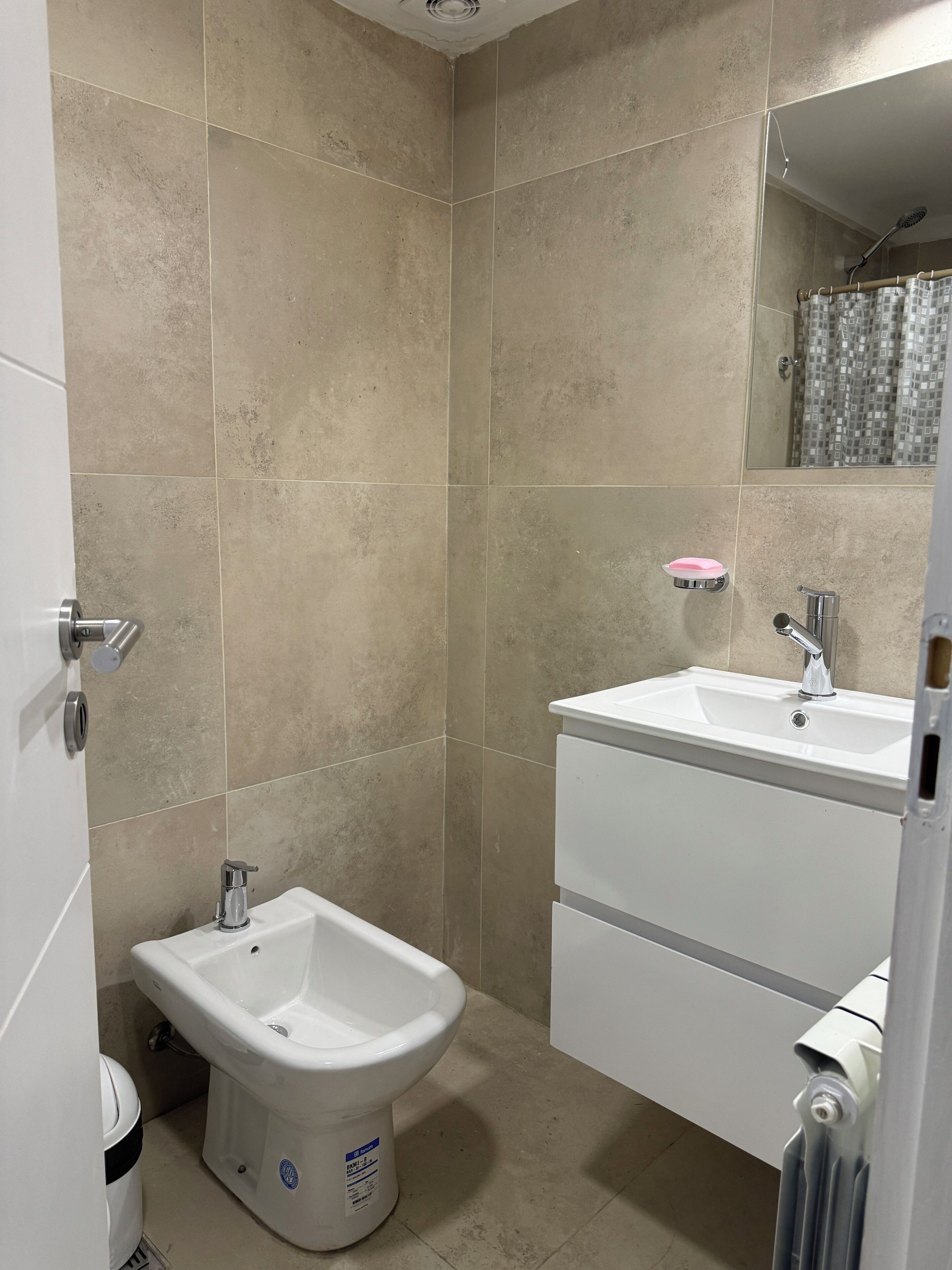 A bathroom with beige tiles, a bidet, a sink, and a mirror.
