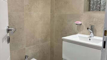 A bathroom with beige tiles, a bidet, a sink, and a mirror.