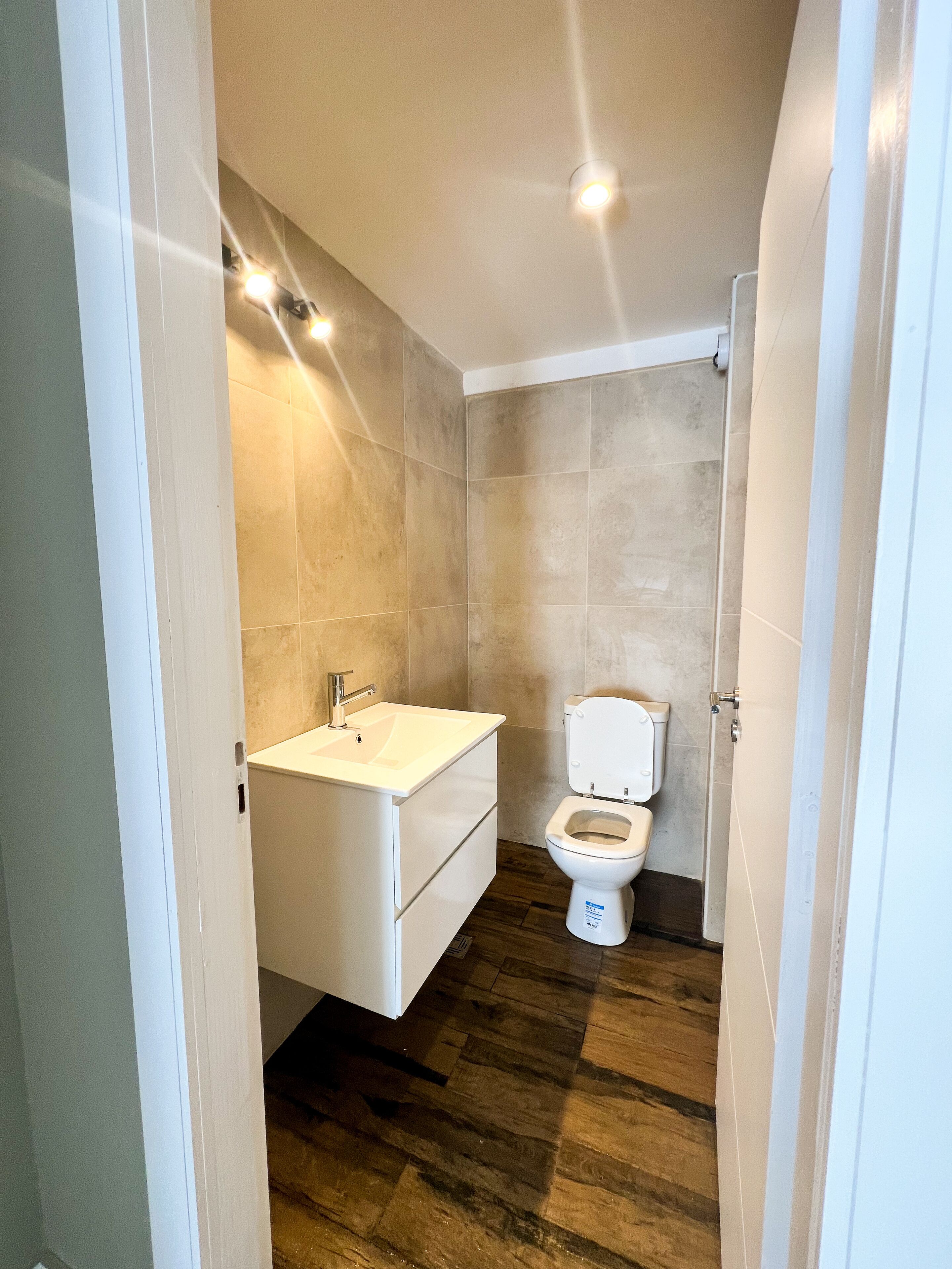 Une petite salle de bain avec un lavabo, des toilettes et une douche, le tout de couleur blanche.