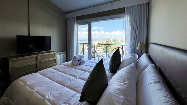 Ein Hotelzimmer mit einem großen Bett, einem Fernseher, einem Balkon mit Aussicht und einem Vorhangfenster.