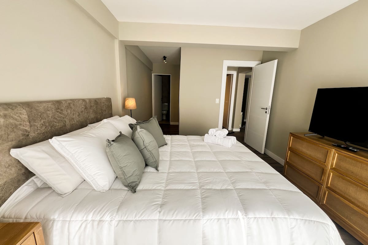 Ein Hotelzimmer mit einem großen Bett, einem Fernseher, einer Holzkommode und einem durch eine offene Tür einsehbaren Badezimmer.