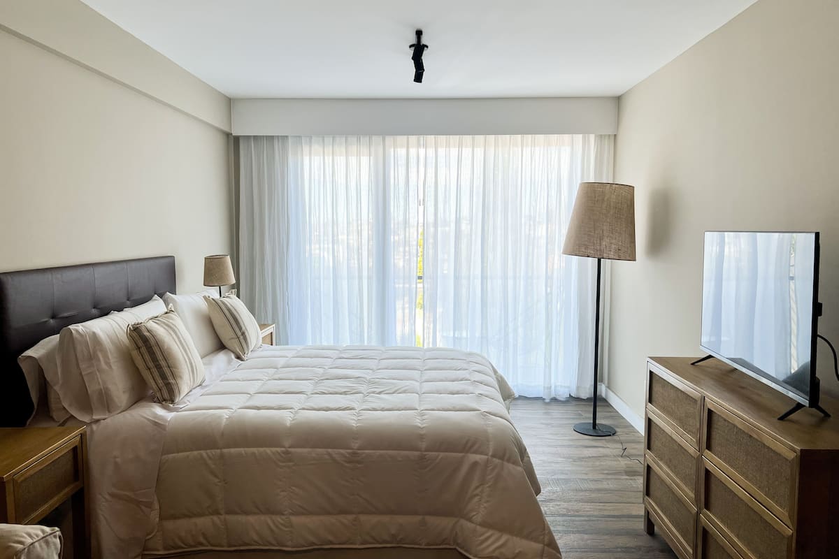 Ein Hotelzimmer mit einem großen Bett, einem Nachttisch mit Lampe, einem Schminktisch und einem Fernseher.