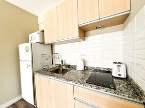 A compact kitchen with wooden cabinets, a built-in oven, a sink, a kettle, and a toaster. - Guemes Apartments (San Carlos de Bariloche)