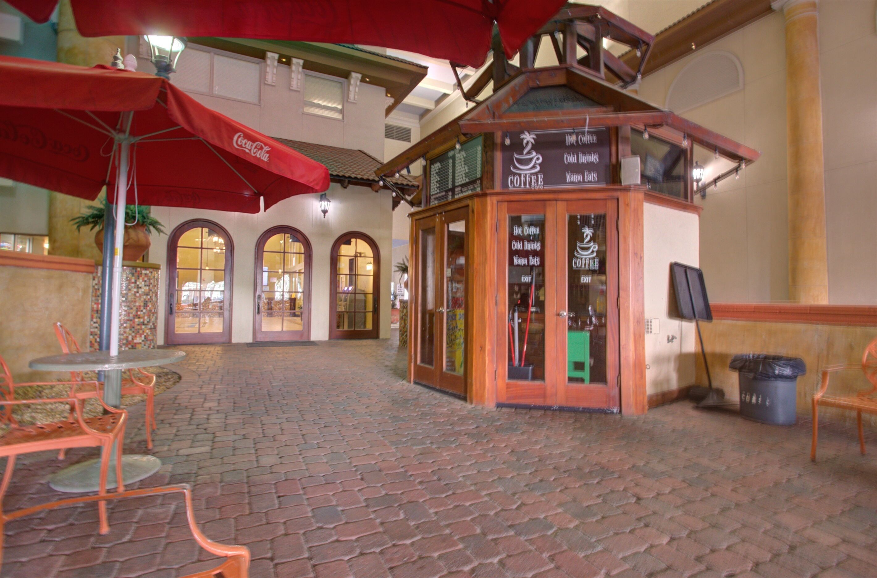 Un patio acogedor con una cafetería, suelo de ladrillo y mobiliario exterior con sombrillas.
