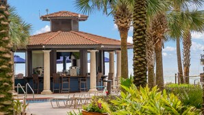 A covered outdoor seating area with a pool, palm trees, and a view of the ocean. - Beachfront Condo • Lagoon Pool • Sleeps 6 (Panama City Beach)