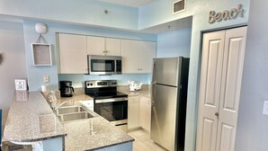 A kitchen with white cabinets, a stainless steel refrigerator, a microwave, an oven, and a granite countertop. - Beachfront Condo • Lagoon Pool • Sleeps 6 (Panama City Beach)