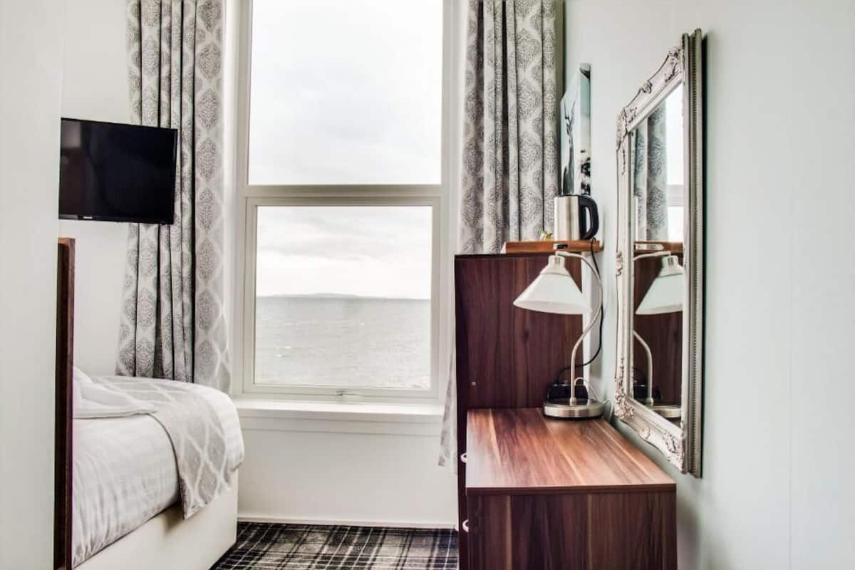 A hotel room with a bed, a desk with a lamp, a mirror, and a TV mounted on the wall.