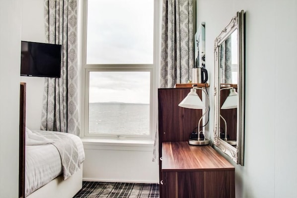 Habitación de hotel con cama, escritorio con lámpara, espejo y televisor en la pared.