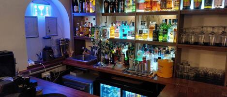 Una zona de bar con estantes llenos de botellas de licores, un fregadero y un mostrador refrigerado.