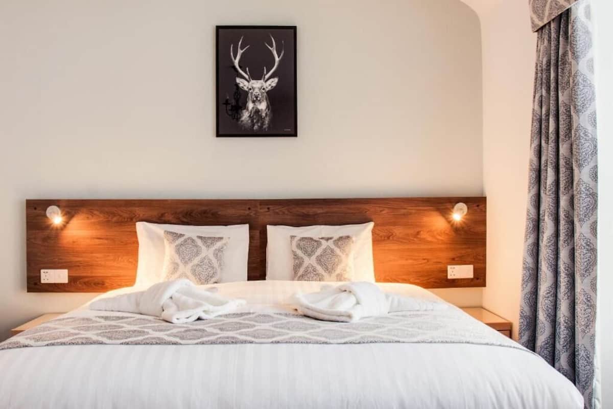 A hotel room with a wooden headboard, two patterned pillows, a framed deer head artwork, and a bed with white linens.