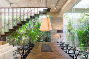 A modern interior with a wooden dining table, black chairs, a staircase with metal railings, and indoor plants.