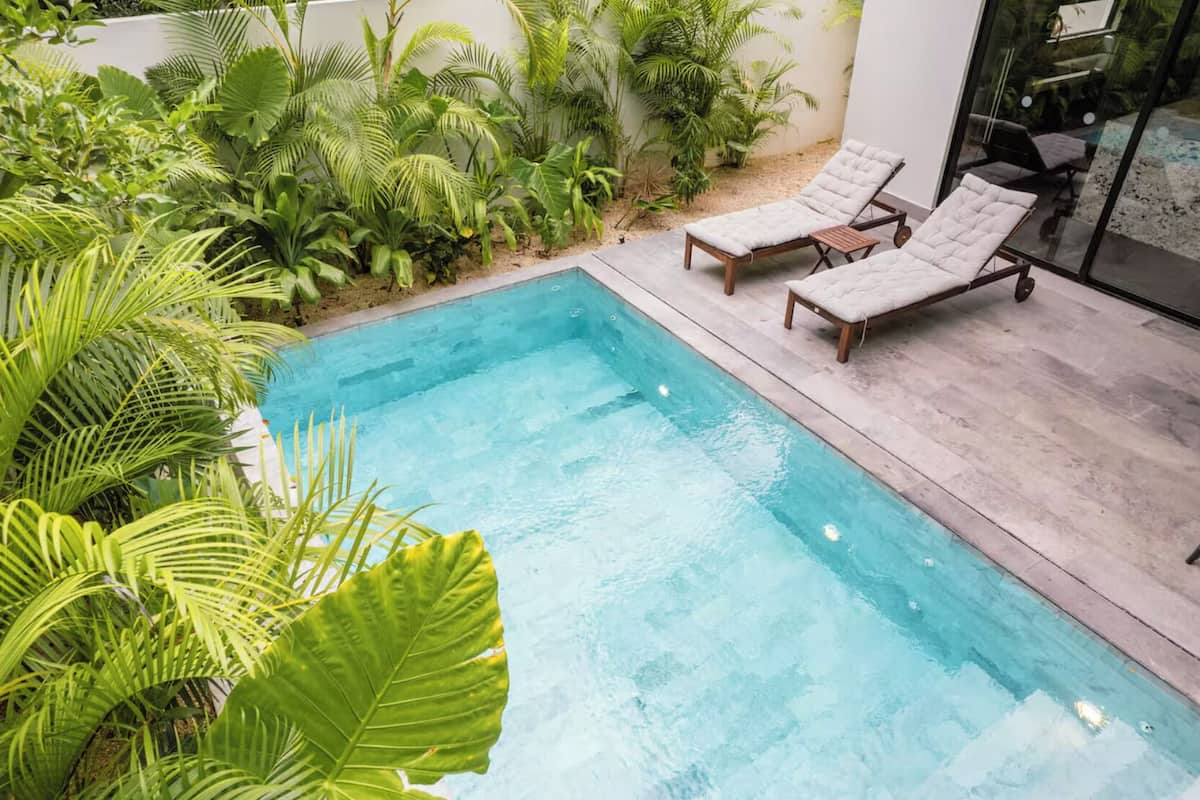 A rectangular swimming pool with two sun loungers and a wooden deck.