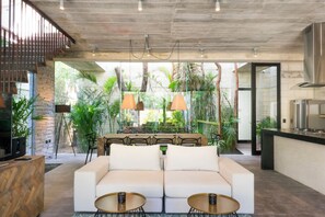 A modern living area with a sofa, two small tables, and a kitchen in the background.